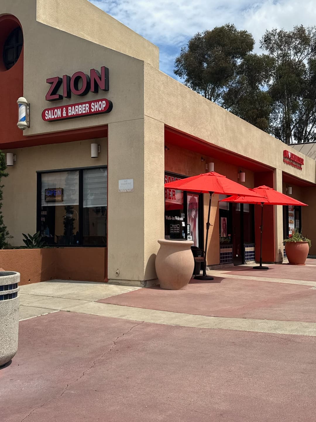 Exterior storefront of Zion Salon & Barber Shop with red umbrellas in National City, California.